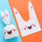 Rabbit-ear gift bag, white with pink flower accents and cartoon bunny face design.