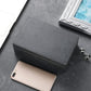 Dark gray stitched phone shielding box with hinged top flap and a phone inside