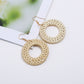 Handmade woven circular hoop earrings with gold-tone ear hooks, natural beige fiber.