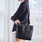 Black messenger bag with top handles and shoulder strap, zip-top and front pocket