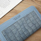 Light blue croc-embossed wallet front with stitched border and small logo patch