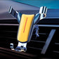Yellow triangular gravity phone holder clipped to car air vent, chrome arms and base supports