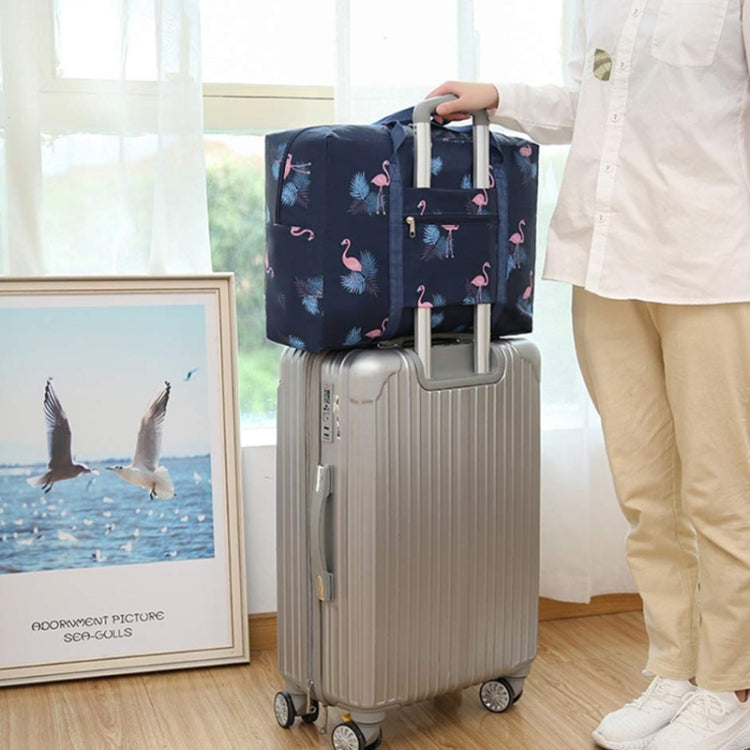 Navy flamingo-pattern foldable luggage bag strapped over a rolling suitcase