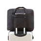 Black trolley storage bag with front zip pocket and top handle, secured over luggage handle