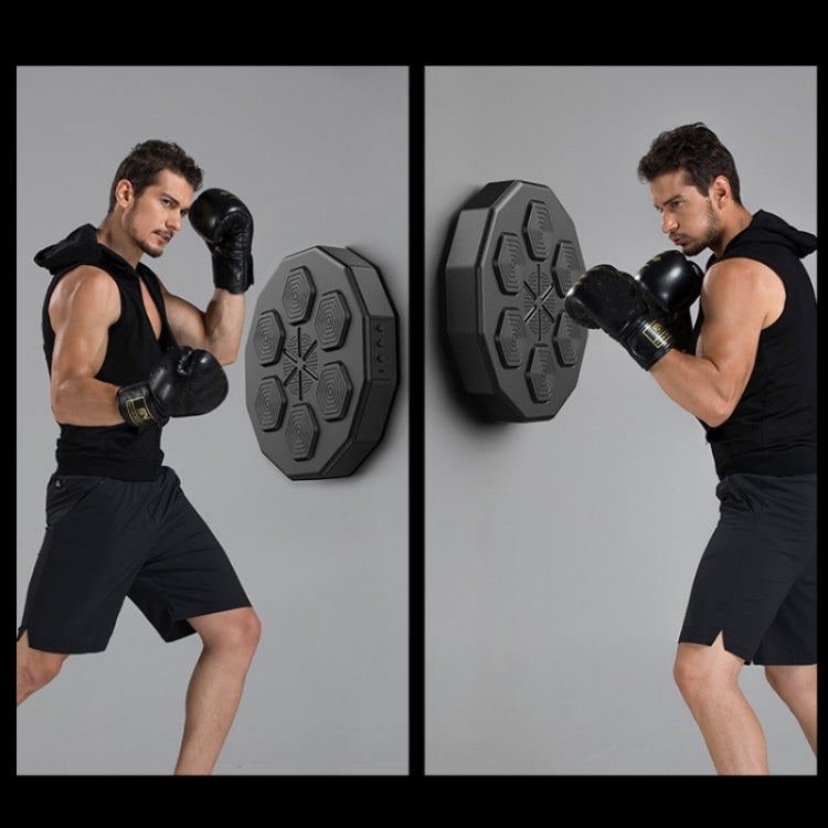 Man practicing boxing hits with black gloves using a wall-mounted electronic trainer