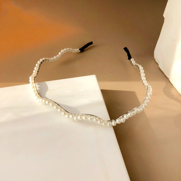 White pearl headband with wavy edge and black grip ends, shown laid on paper
