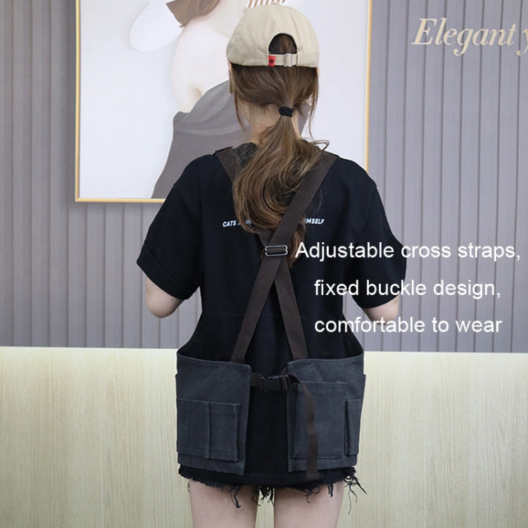 Black canvas tool apron with adjustable cross straps and multiple front utility pockets