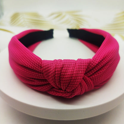 Wide knotted headband in bright pink knit fabric with dark inner backing.