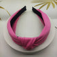 Wide knotted headband in bright pink knit fabric with dark inner backing.