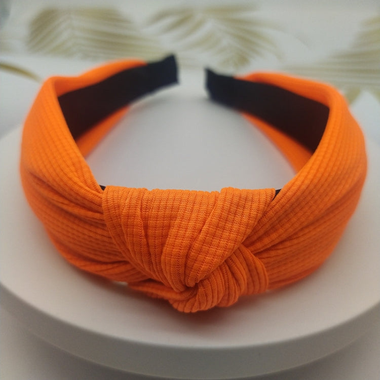 Wide knotted headband in orange knit fabric with dark inner backing.