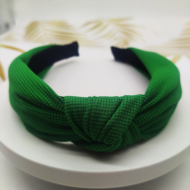 Wide knotted headband in green knit fabric with dark inner backing.