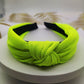 Wide knotted headband in fluorescent yellow-green knit fabric with dark inner backing.