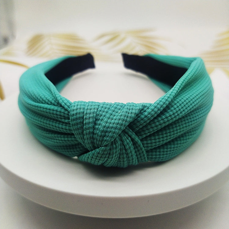 Wide knotted headband in teal knit fabric with dark inner backing.