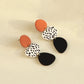 Dangle earrings: orange disc, leopard print oval, and black teardrop drop, side view