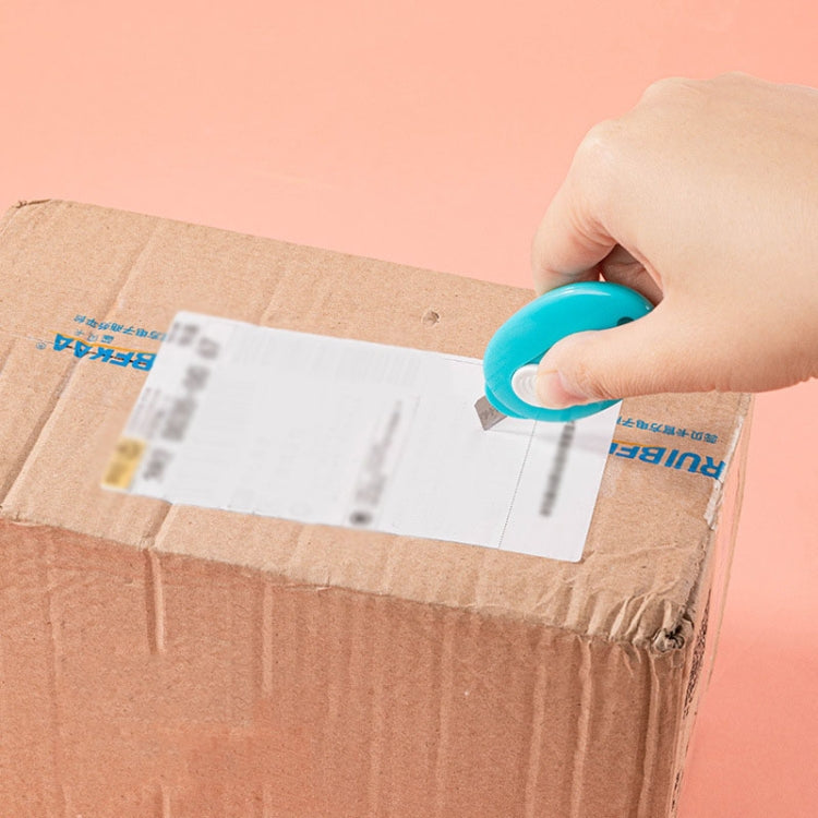 Blue mini utility knife held by hand, blade extended to cut a cardboard package.