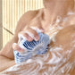 Blue silicone shower scrubber brush with circular fins scrubbing soapy skin