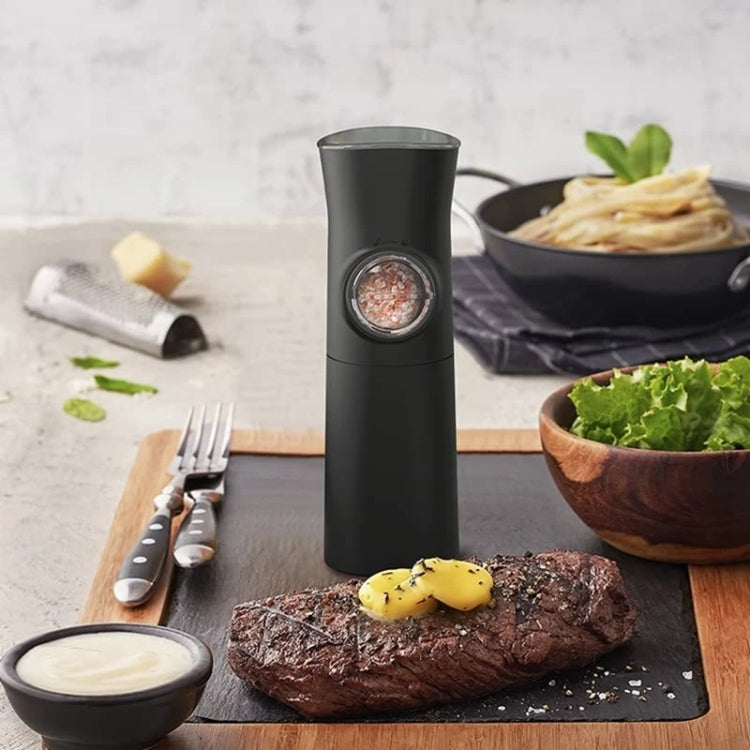 Black electric salt and pepper grinder with LED-lit grinding chamber on a table