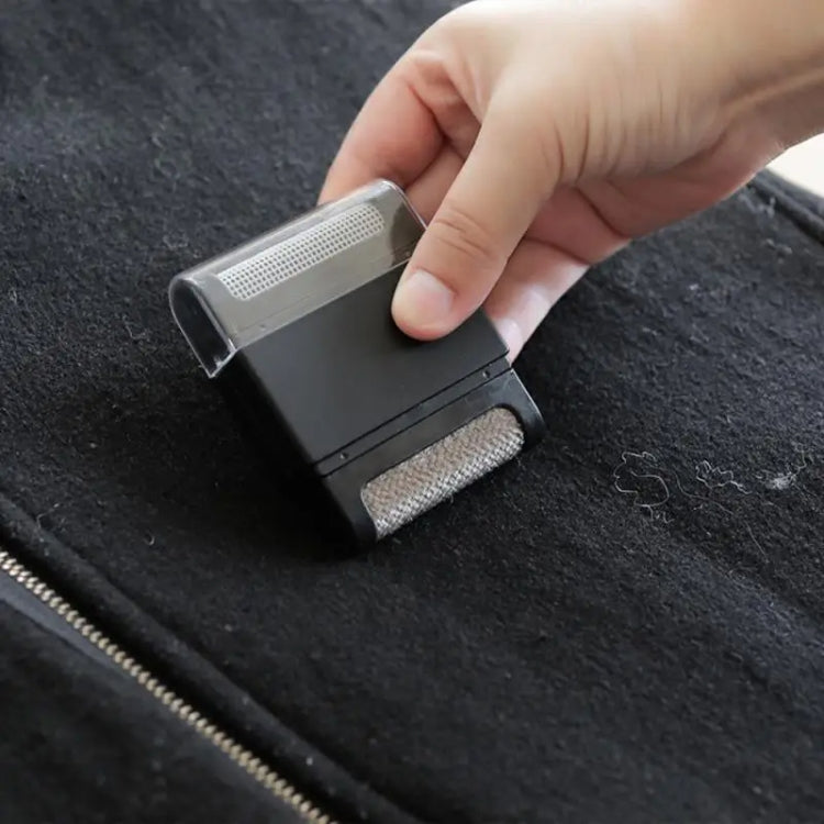 Handheld clothing ball trimmer with metal mesh and textured lint-removal pad on fabric