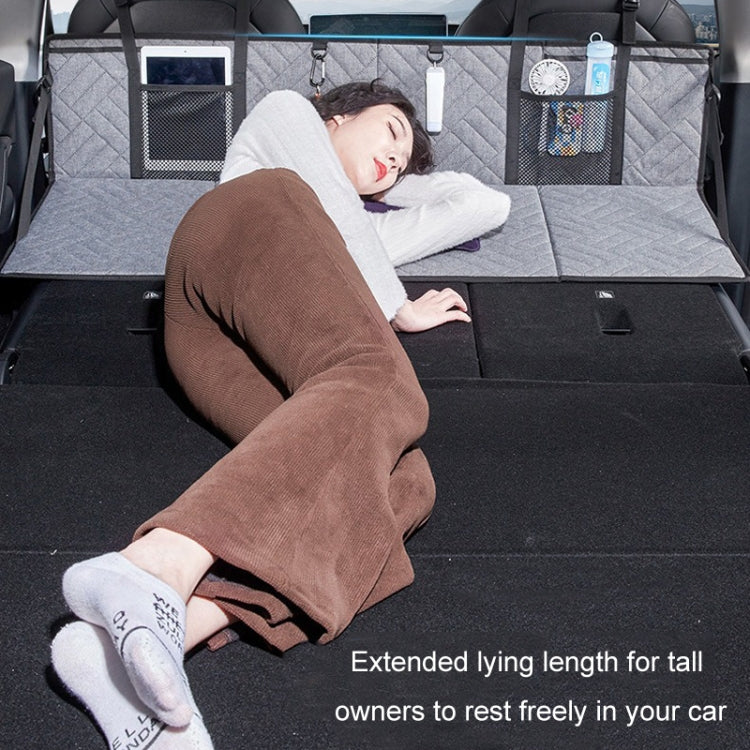Extended car camping bed extension board with quilted surface and storage pockets, person resting
