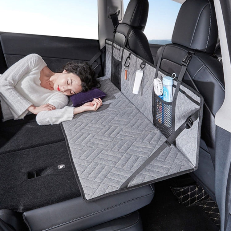 Car camping bed extension board with quilted gray mattress and front storage organizer, person resting