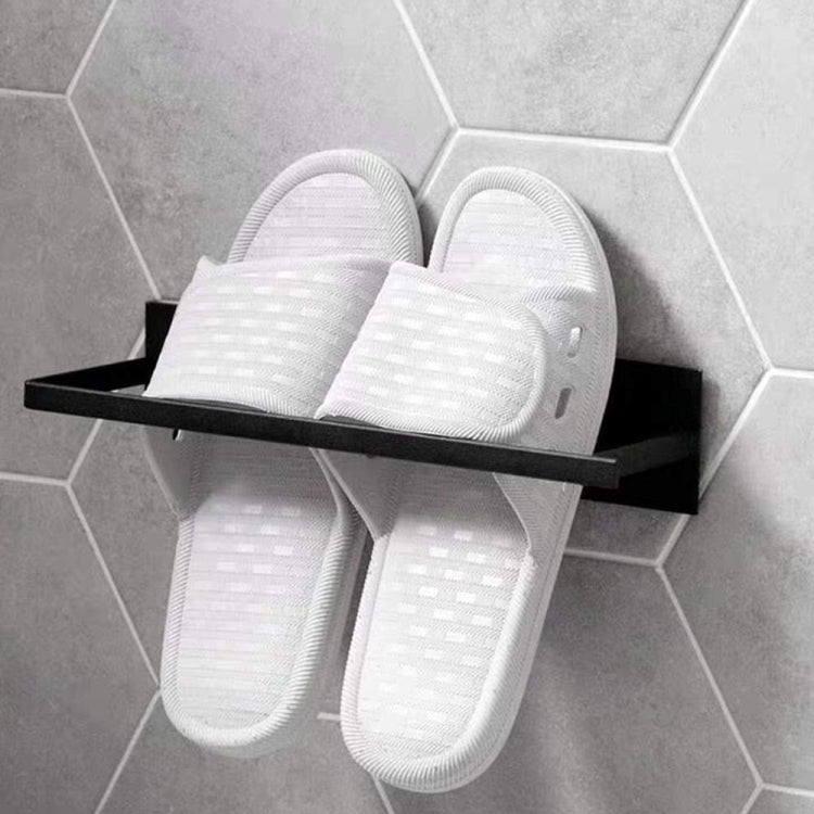 Wall-mounted metal rack with black shelf holding a pair of white slide slippers