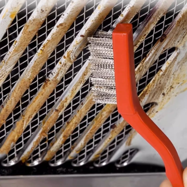 Orange-handled brush cleaning grime from a metal vent or grill grate.