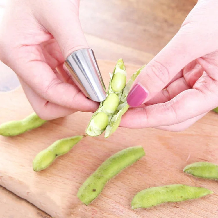 Stainless steel hand guard used to peel green pods on a wooden cutting board