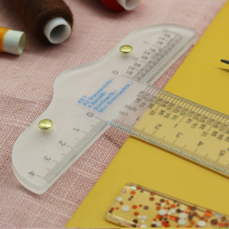 Clear plastic T-square ruler on paper with printed measurement scale and gold pins