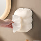 Cream cloud tissue holder mounted on wall; hand pulls tissue from front opening