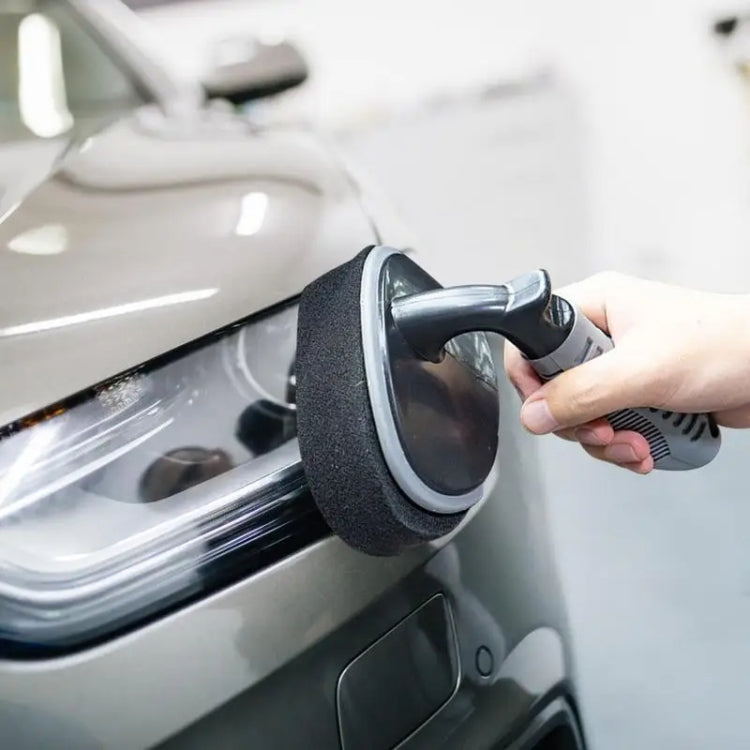 Car waxing sponge brush in use, black foam pad scrubbing a vehicle surface