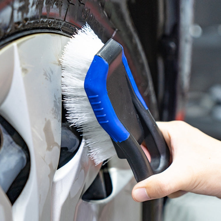 Car tire cleaning brush with stiff white bristles and blue handle, held near wheel
