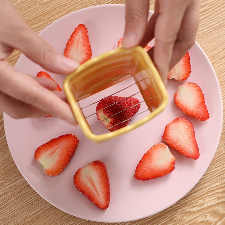 Hand using yellow cup slicer to cut strawberries into slices on a plate