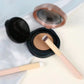 Concealer brush with beige bristles applying makeup from a compact lid
