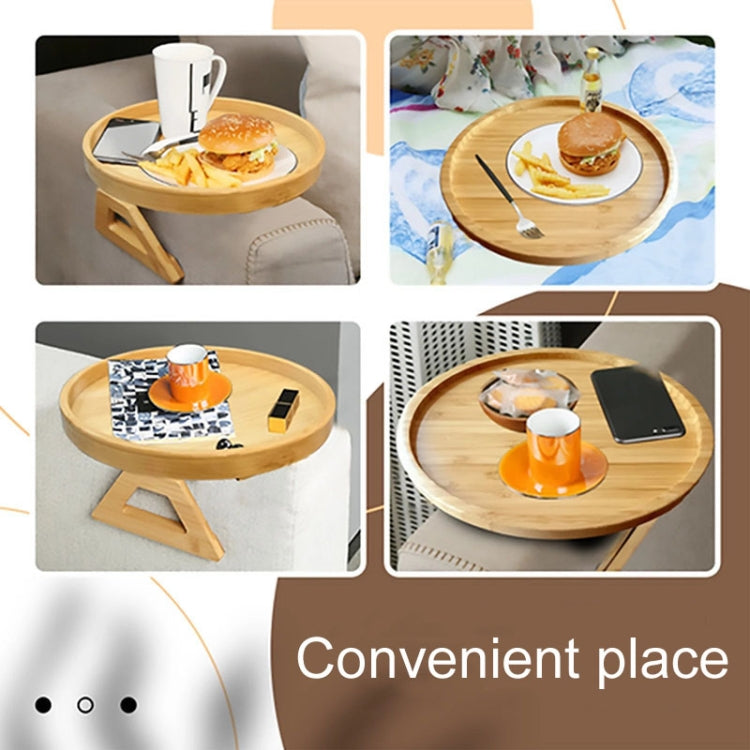 Round wooden serving tray on foldable legs with coffee cups on a sofa arm.