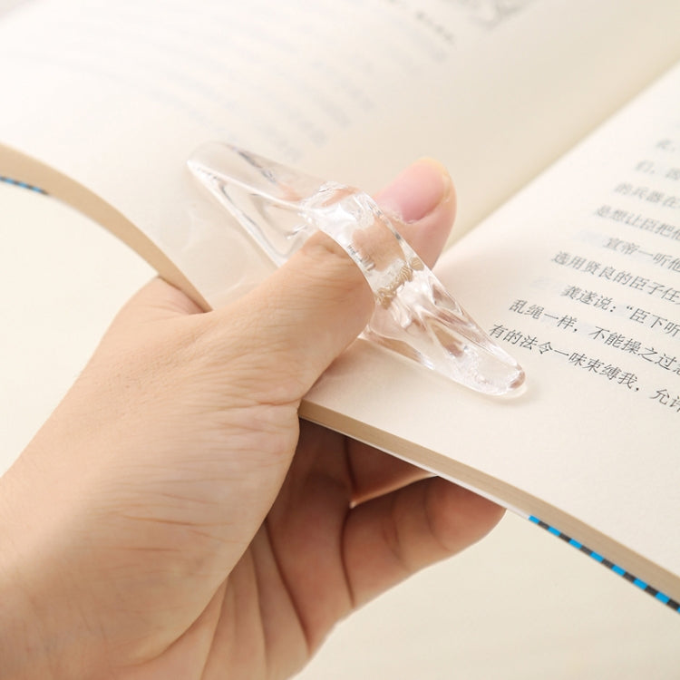 Hand holding a transparent acrylic thumb bookmark on the edge of an open book.