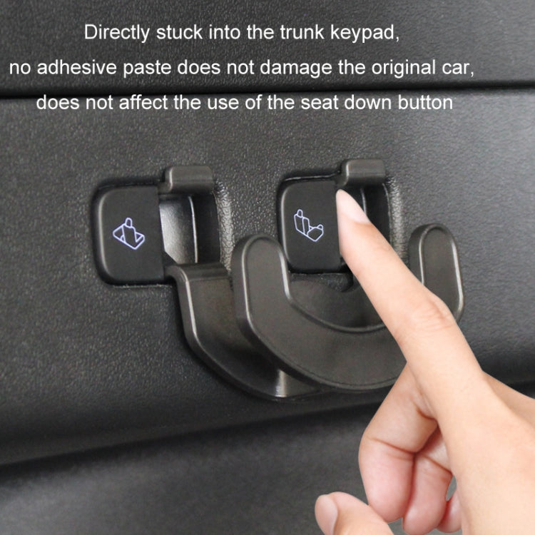 Black trunk seat button hook attached to trunk keypad, finger pressing into place.