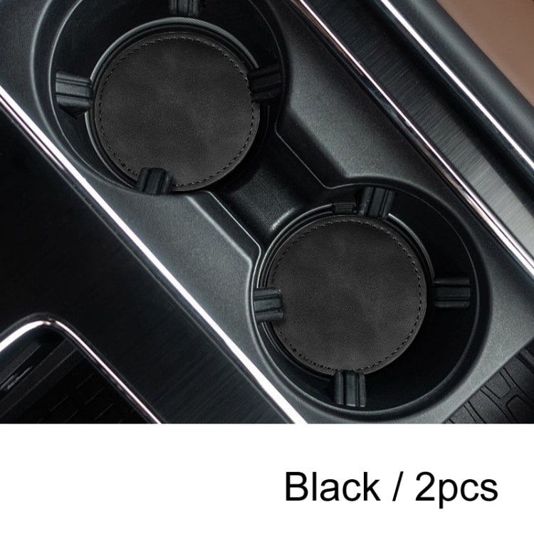 Set of 2 round black suede anti-slip coasters in a car center console tray.