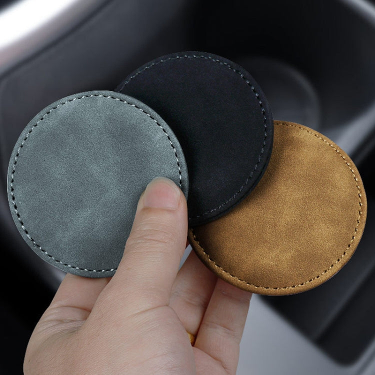 Close-up of round suede coasters in gray and black with stitched rim, handheld.