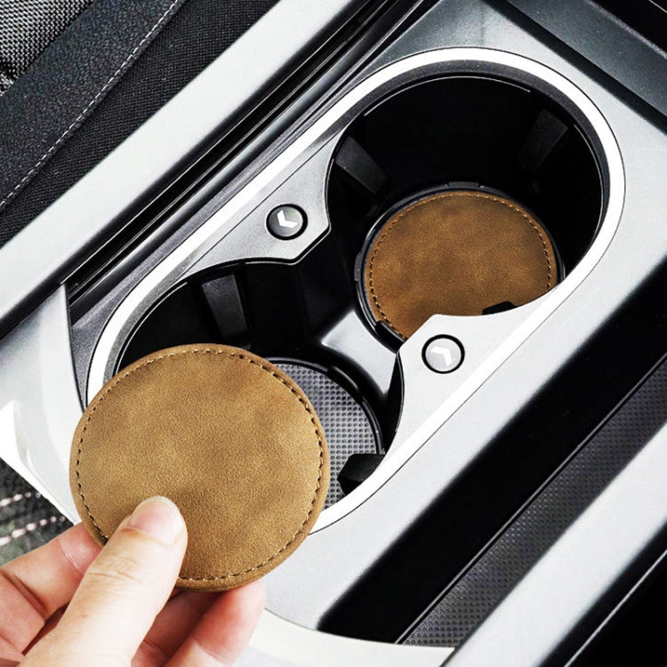 Set of 2 round brown suede anti-slip coasters in car cup holders, one lifted.