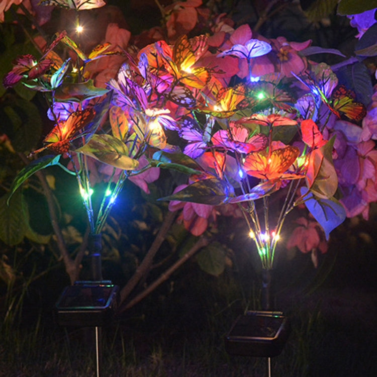 Multiple butterfly flower solar ground lights glowing at night in a garden