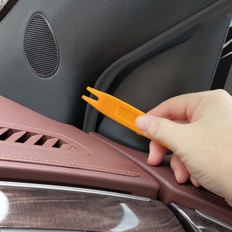Orange pry tool removing car interior trim near door speaker
