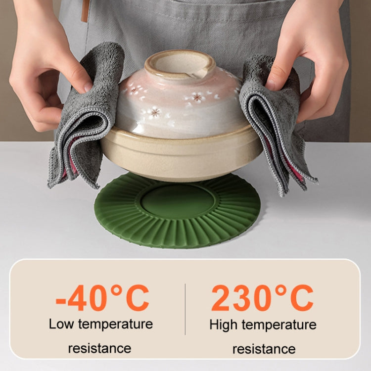 Green silicone heat insulation mat under a hot pot, with folded towels on top.