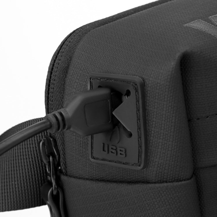 Close-up of dark men’s crossbody bag side port with attached cable and embossed logo