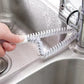 White crevice cleaning brush scrubbing a sink edge near the faucet