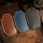 Set of three leather key fob covers in brown, blue, and dark gray with textured grip