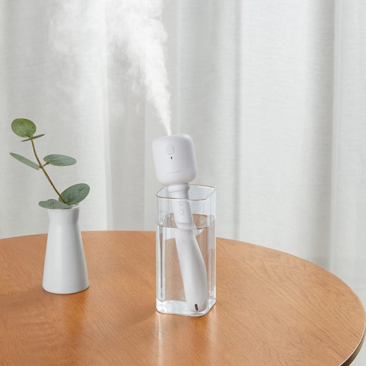 White mini humidifier misting into a clear glass cup
