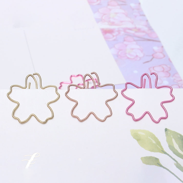 Three sakura-shaped metal paper clips in gold, rose gold, and pink on stationery