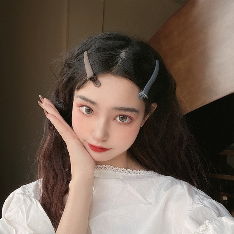 Light gray duckbill hair clip holding side bangs on dark hair.