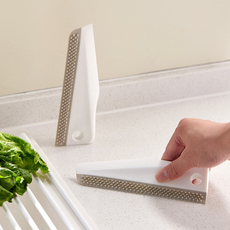 Manual cleaning scraper with perforated brush edge being used on a countertop