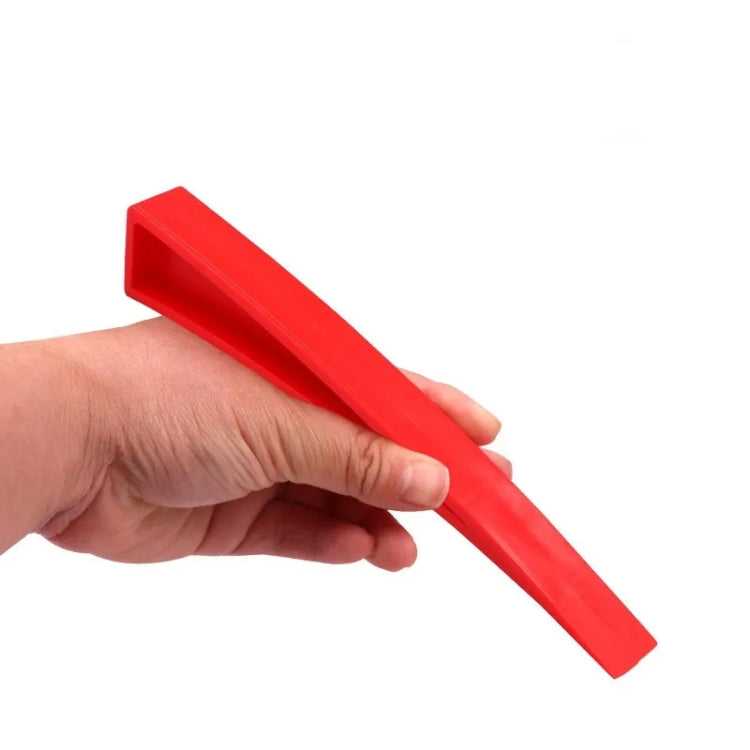 Red plastic car dent repair support clip held in hand, long wedge shape